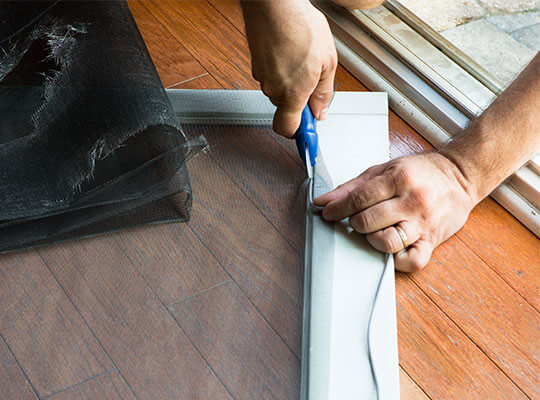 Hands of person cutting a new screen for an old door.